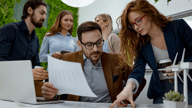 Professionals collaborating at a desk with documents in a modern office with greenery.