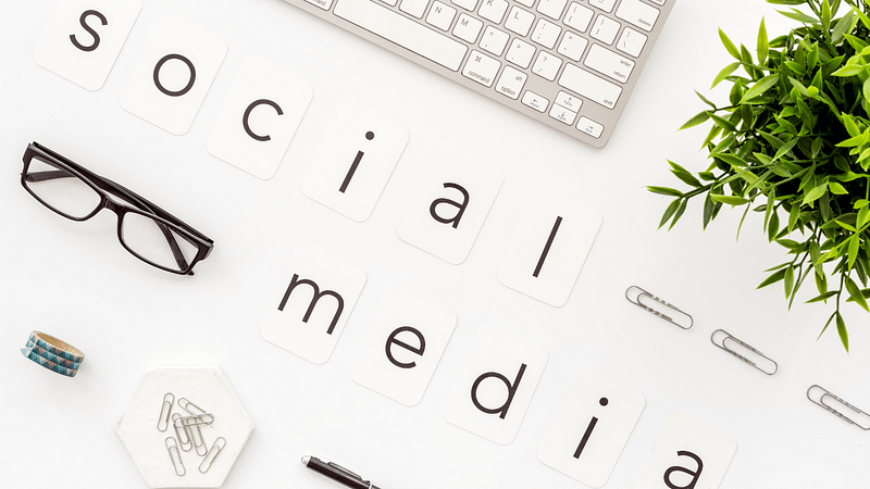 Flat lay of a workspace with keyboard, glasses, "social media" letters, and a potted plant.