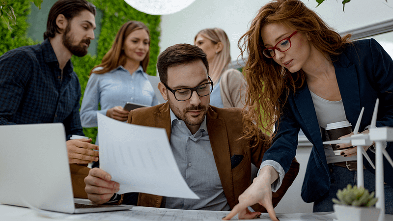 Professionals collaborating at a desk with documents in a modern office with greenery.