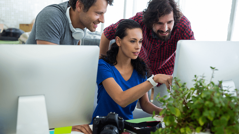 Diverse young adults collaborating at a workspace with computers, plants, and a camera.